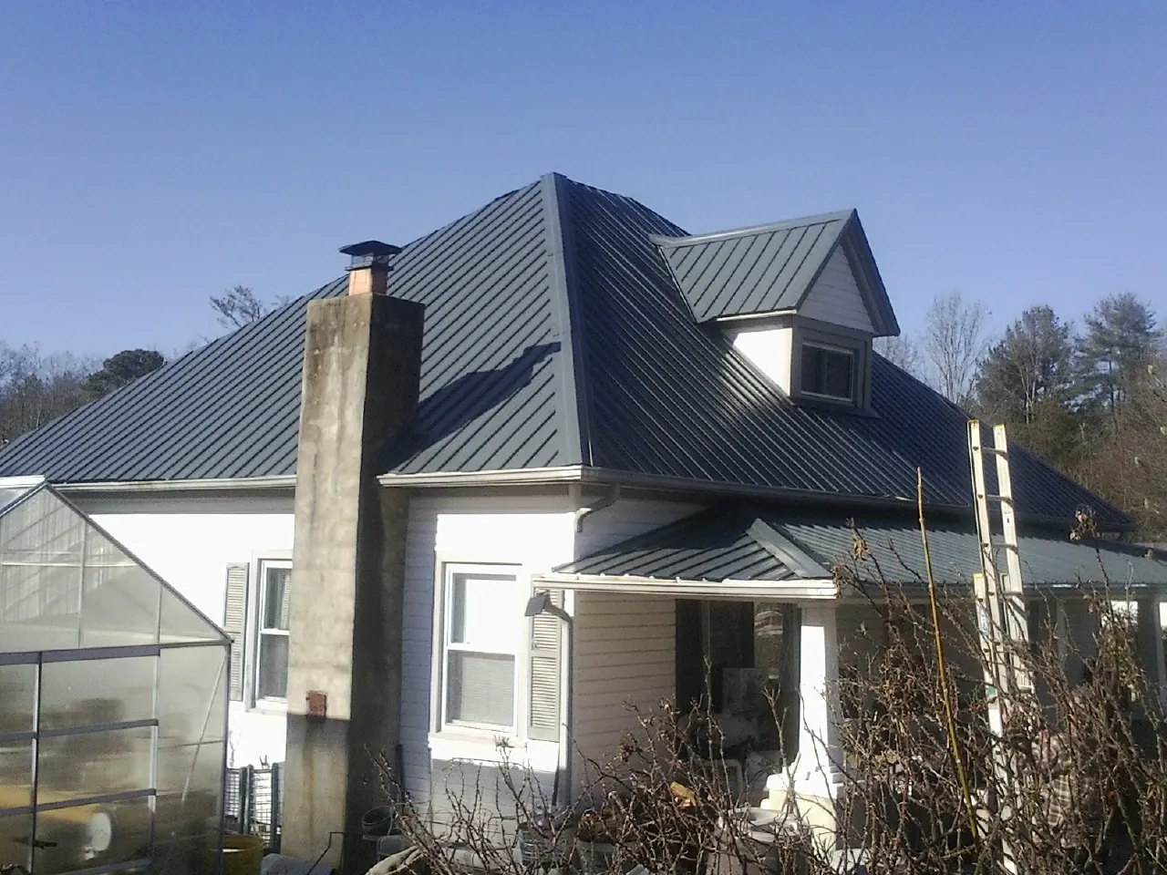 Dark blue standing seam metal roof on a white farmhouse with dormer — Slate & Tile Roof Repair by Roofing Brothers in Lenexa