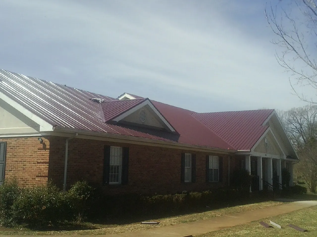 Red metal roof with gabled entries on a long brick building, from a Hail Damage Roof Repair job in Lenexa