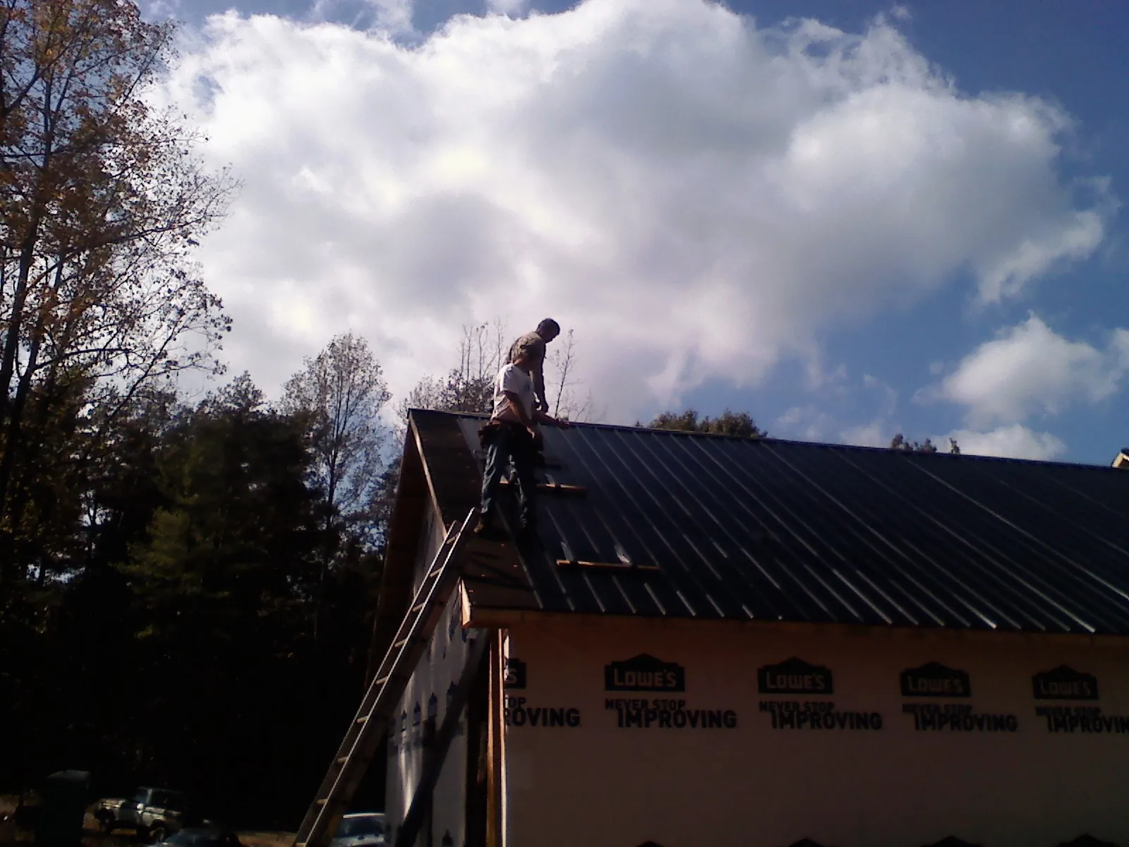 Roofer fastening dark metal panels high against a cloudy sky, from a Roof Inspection job in Lenexa