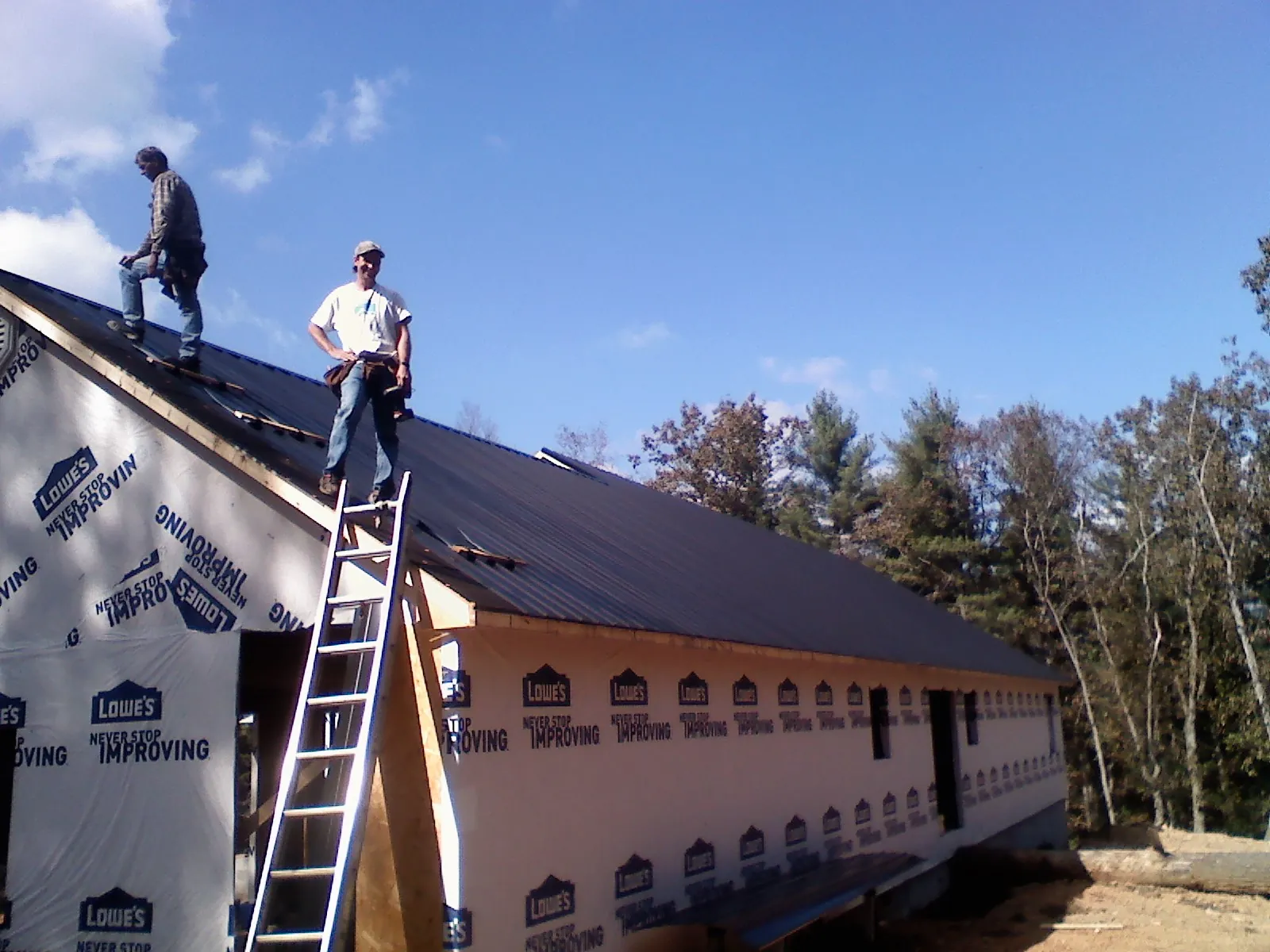 Two roofers standing on a long dark metal roof over a wrapped building in Lenexa